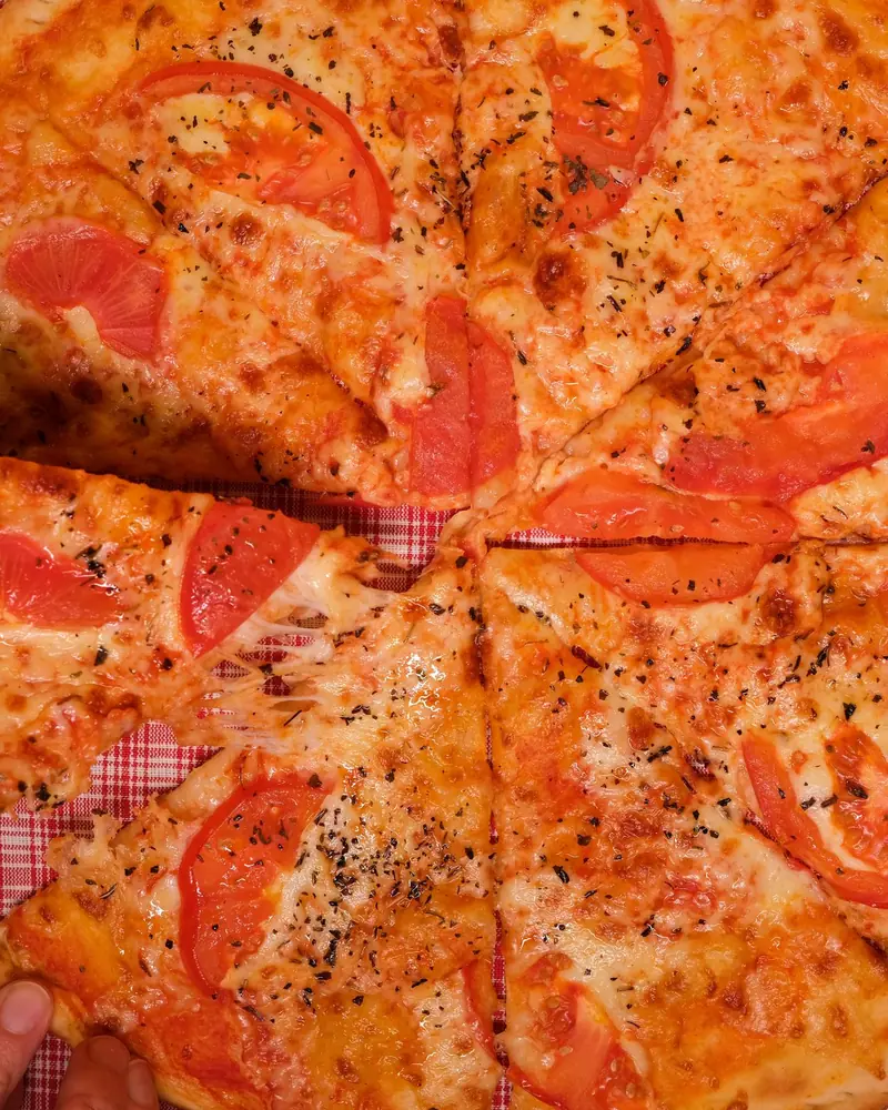 Dłoń bierze kawałek pizzy z kraciastego obrusu